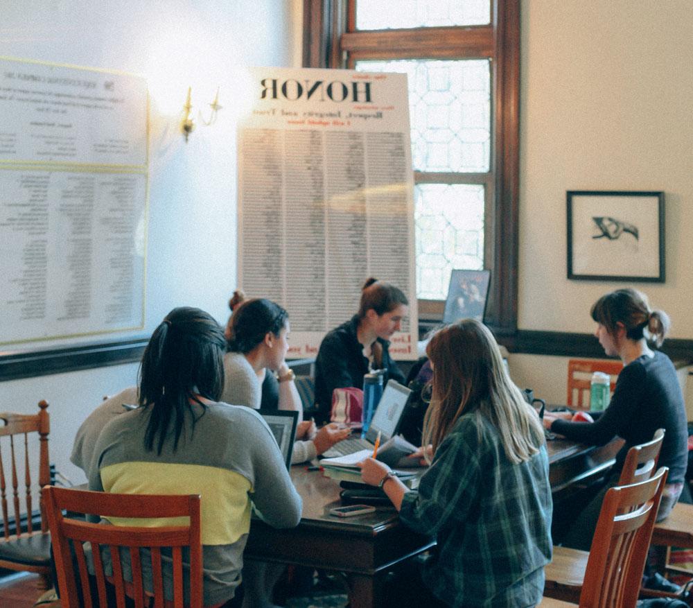 students sitting around table in gallery with the honor code signed by all hanging behind them